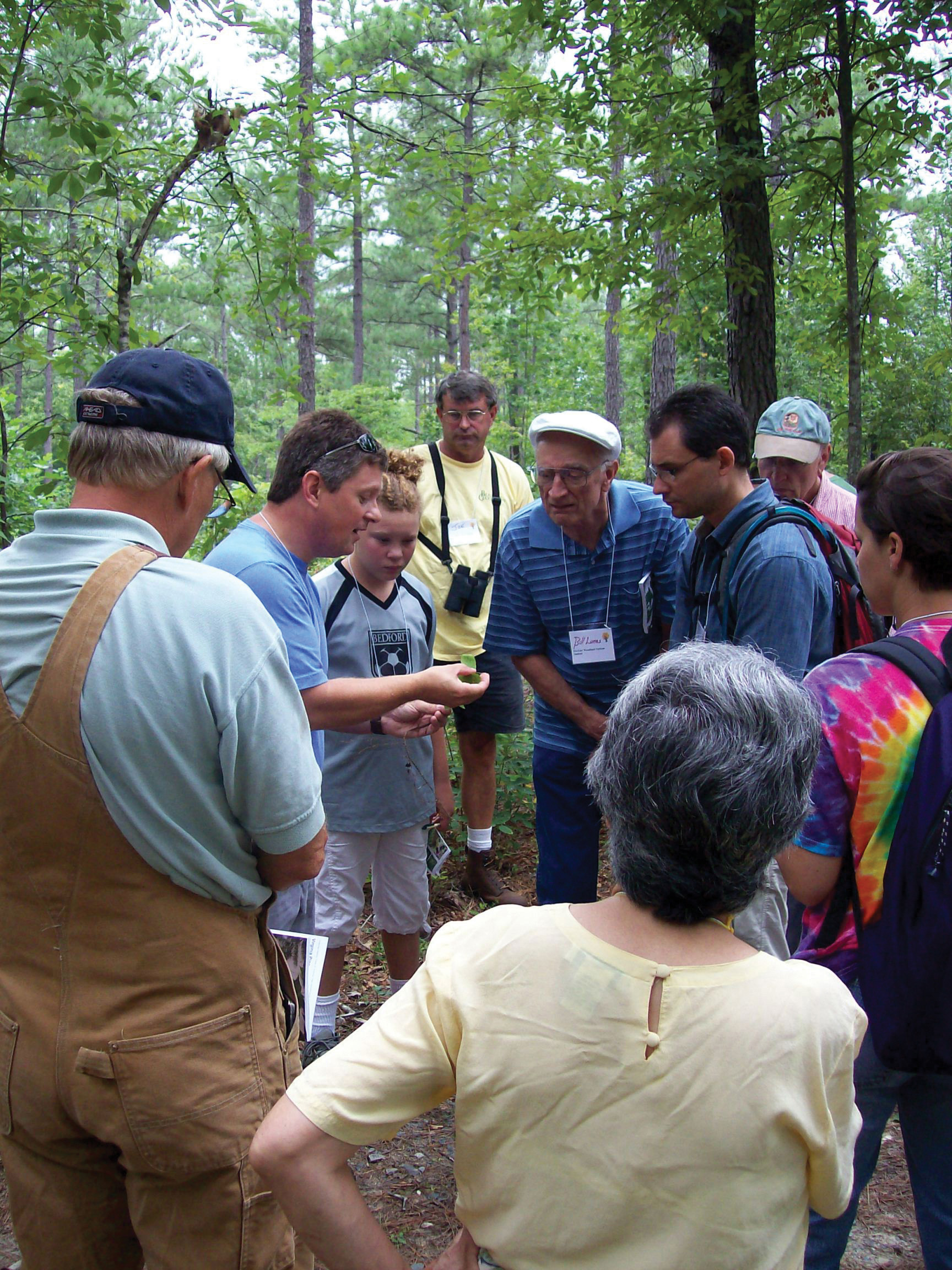 A group of people in a forest looking at a leaf held by an instructor.