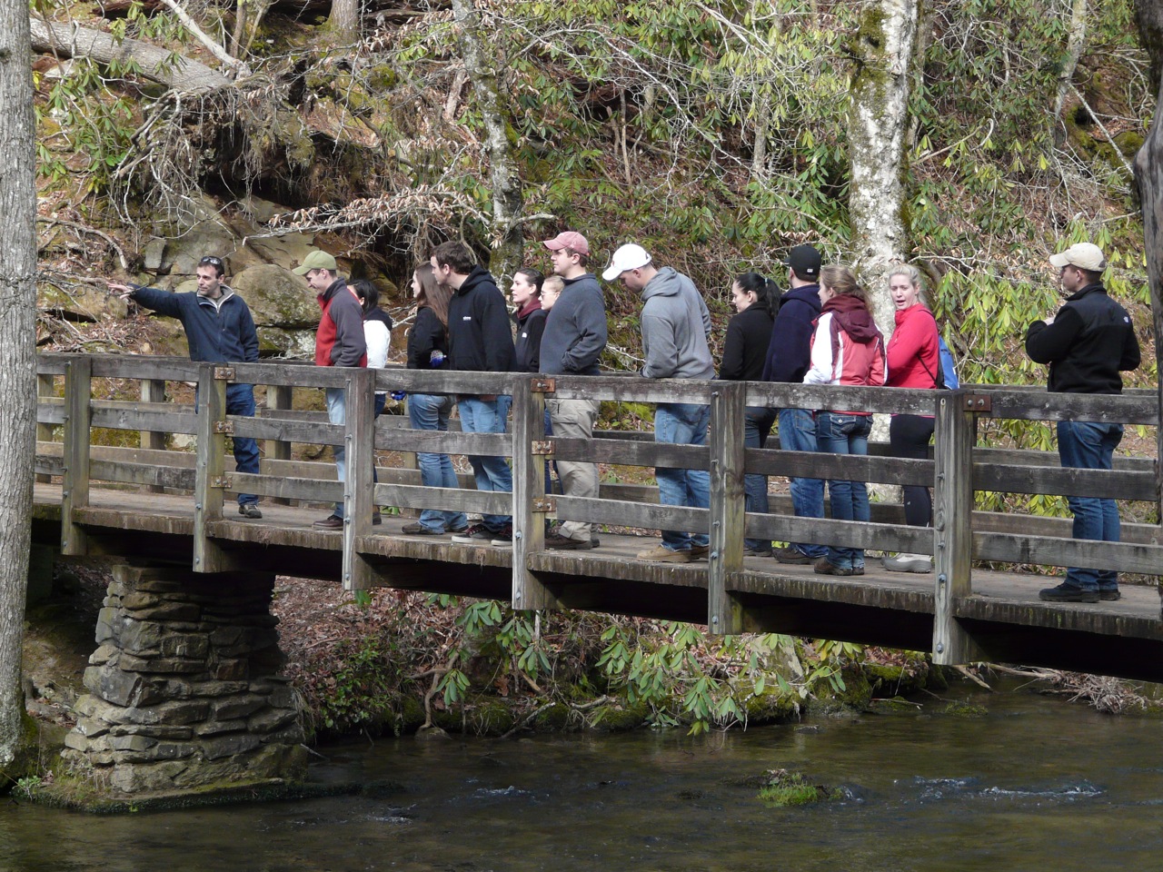 A group of people standing on a wooden footbridge over a creek.