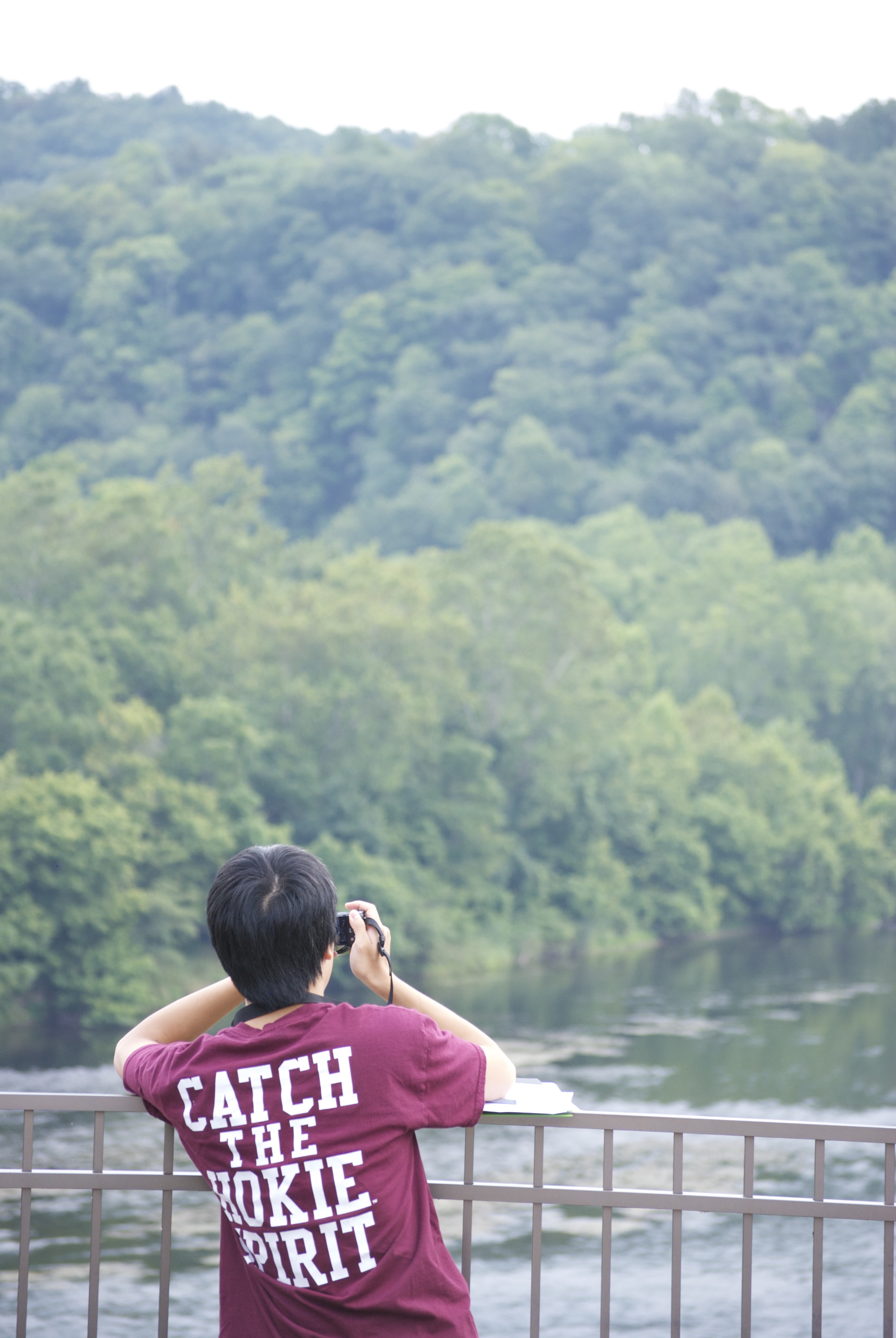 Student stands on a bridge overlooking a river and takes a picture