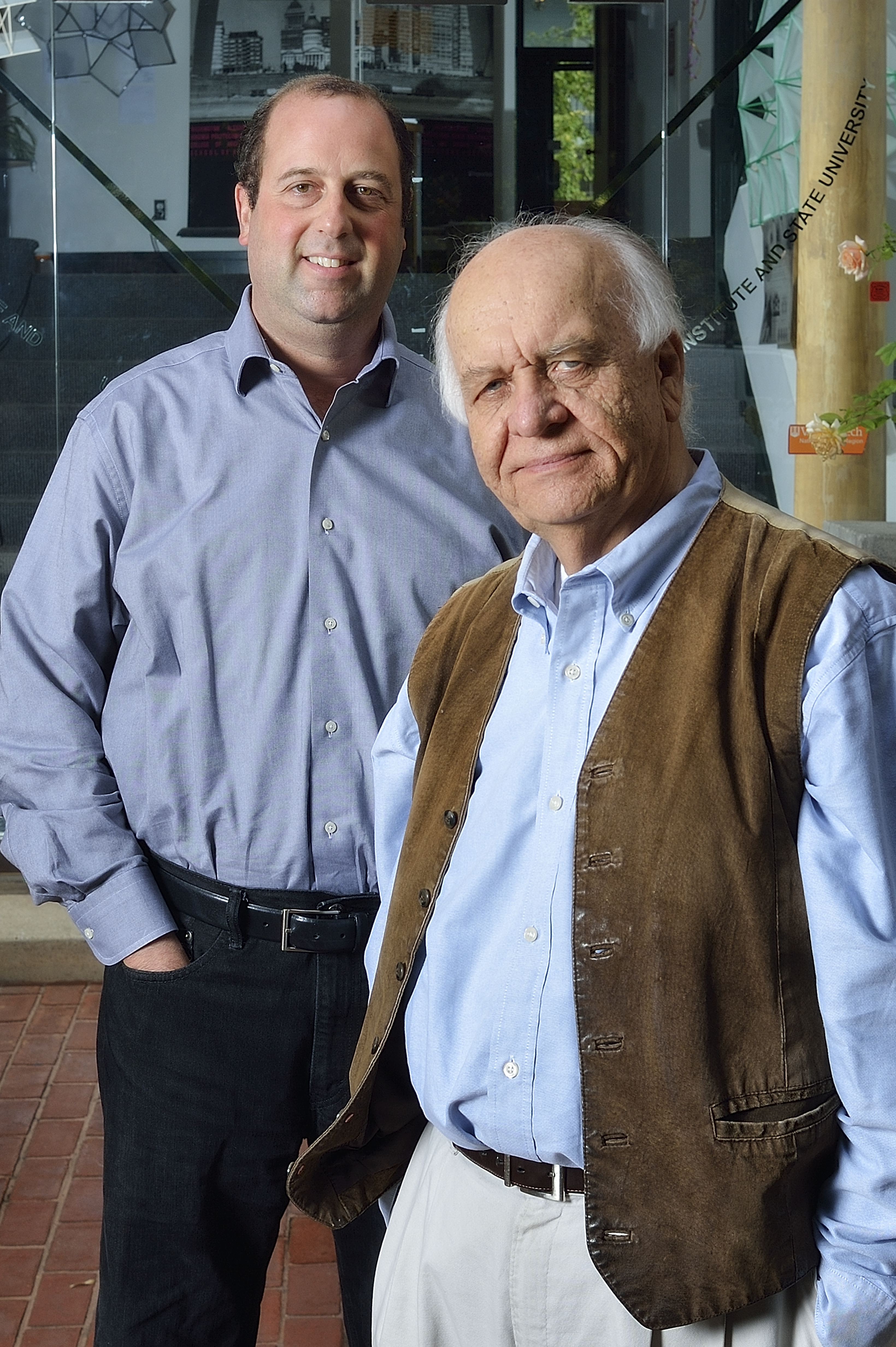 Henry Hollander and Jaan hold standing in front of the glass doors and brick building of the washington-alexandria architecture center