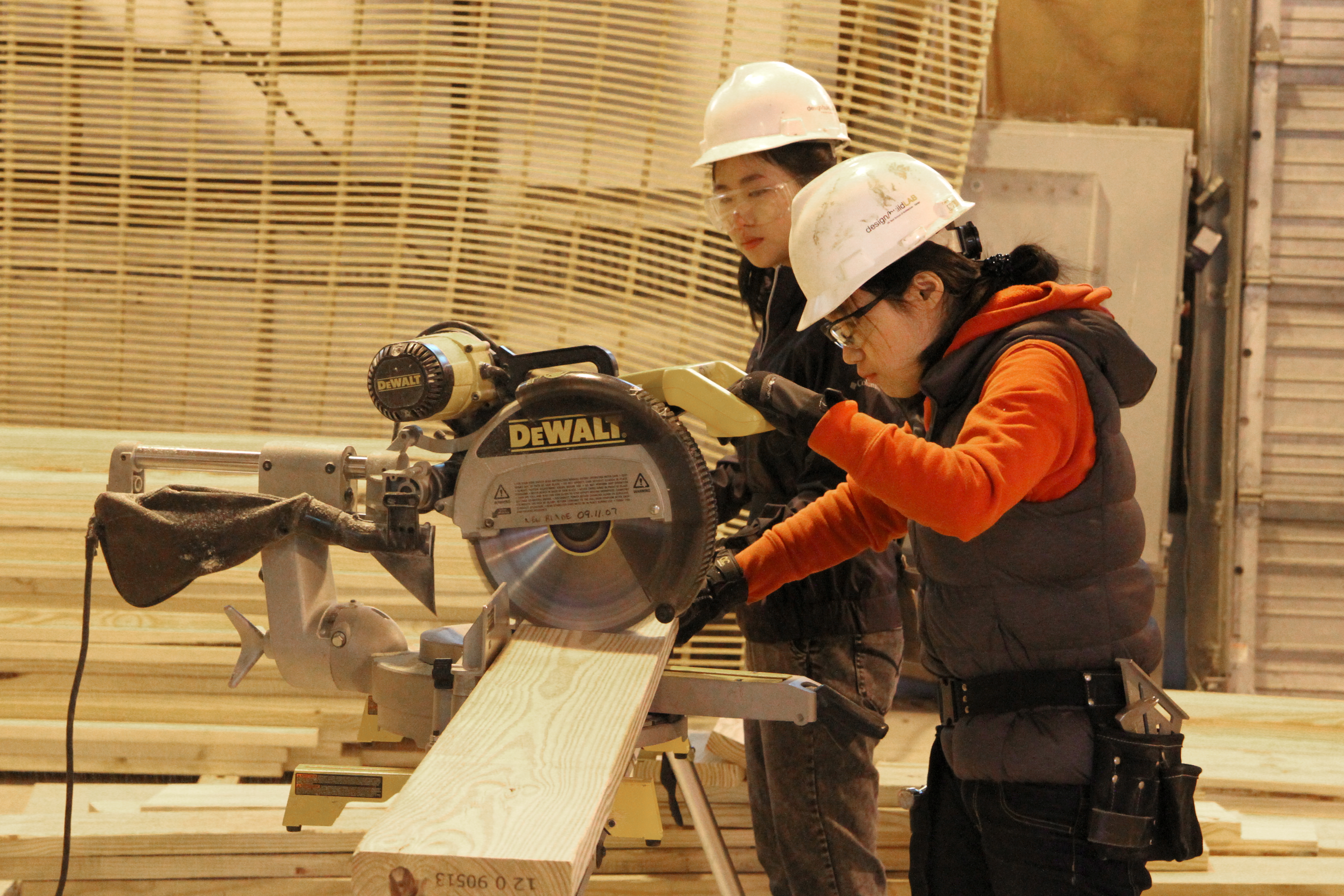 Two students cutting a board with a circular saw. 