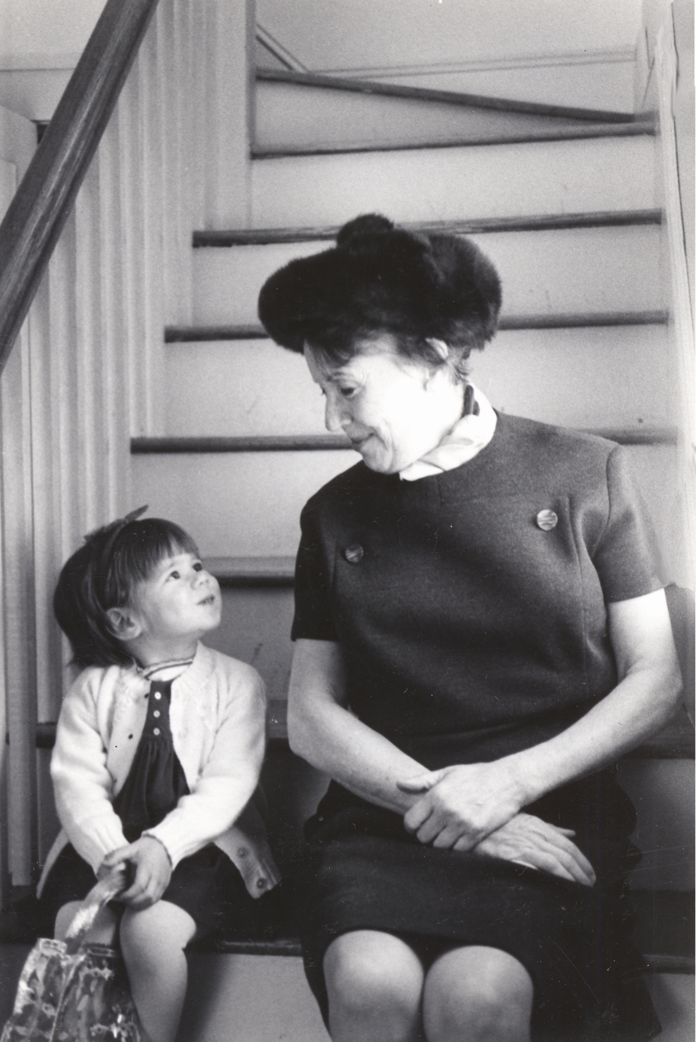 A small child sits next to her grandmother on the stairs in an old black and white photo. 