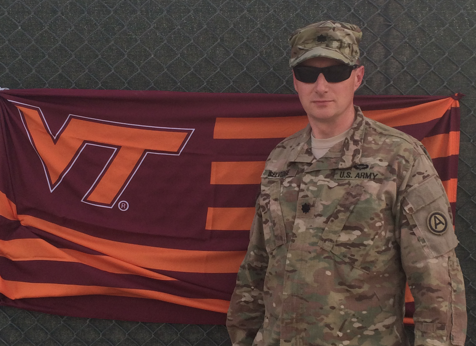 Lt. Col. Roy Selvidge, U.S. Army, Virginia Tech Corps of Cadets Class of 1993 standing in front of a VT flag.