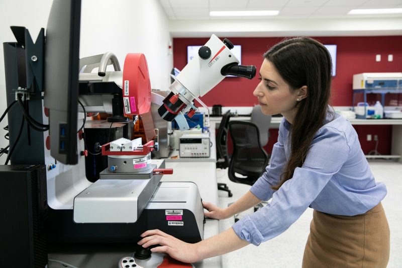 Woman wearing blue blouse standing over microscope in lab