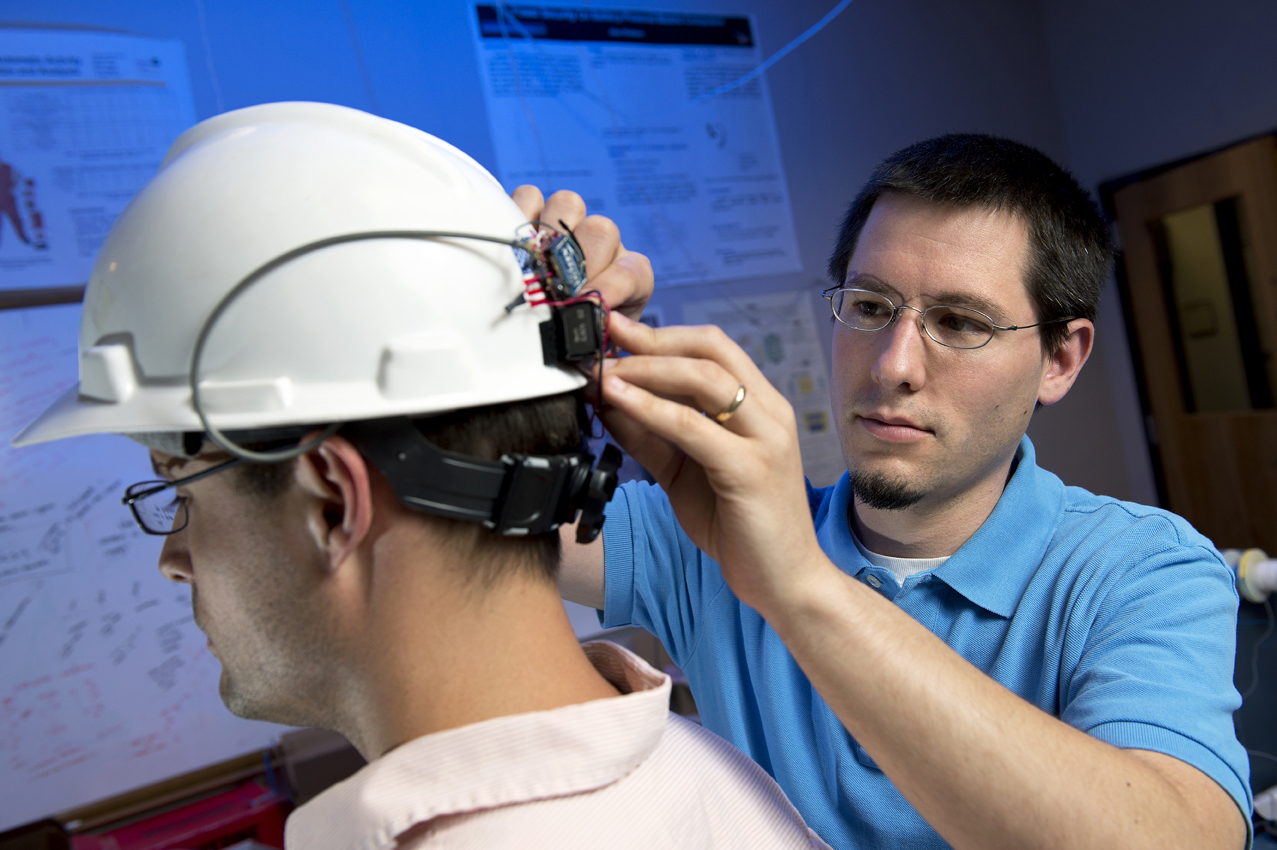 Jason B. Forsyth, right, places a wearable computing system on a helmet worn by the person on the left.